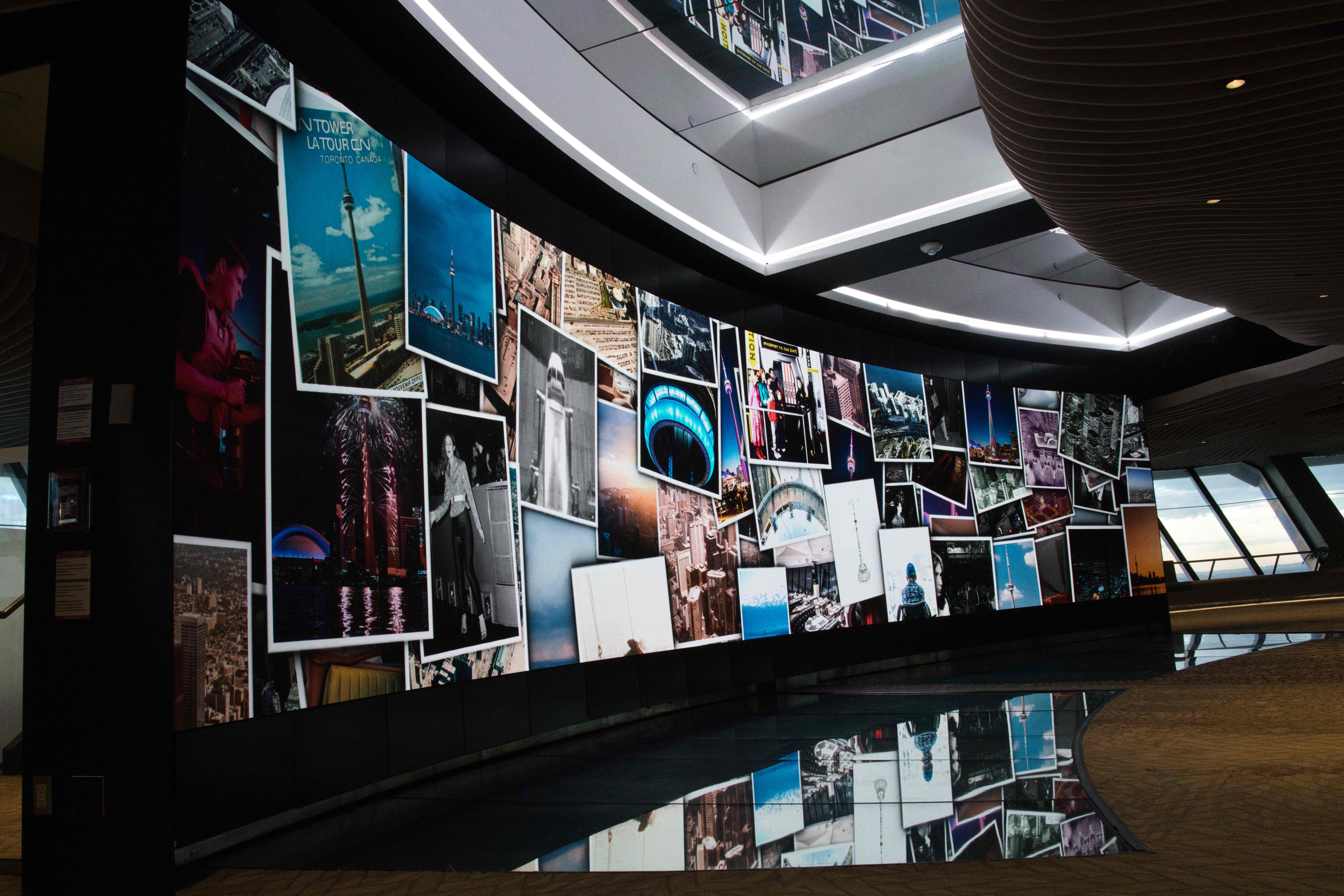 Curved video wall showing a collage of CN Tower photographs, reflected in a dark floor
